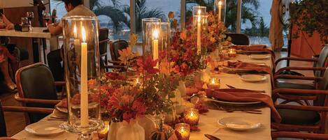 A dining table set for a meal with candles, autumn leaves, and a view of the ocean.