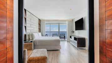 Una habitación de hotel moderna con una cama grande, un espacio para sentarse, un televisor de pantalla plana y vistas al mar.