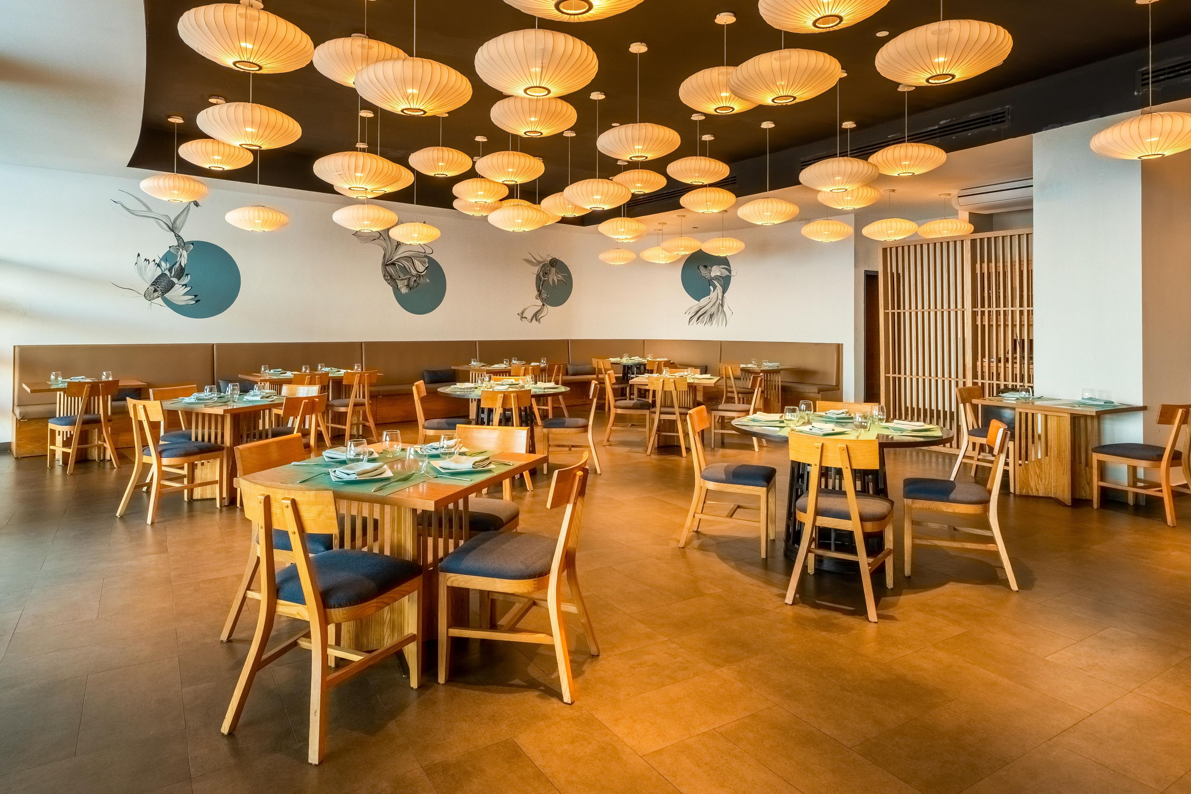 A restaurant interior with multiple tables and chairs, hanging lanterns, and wall art.