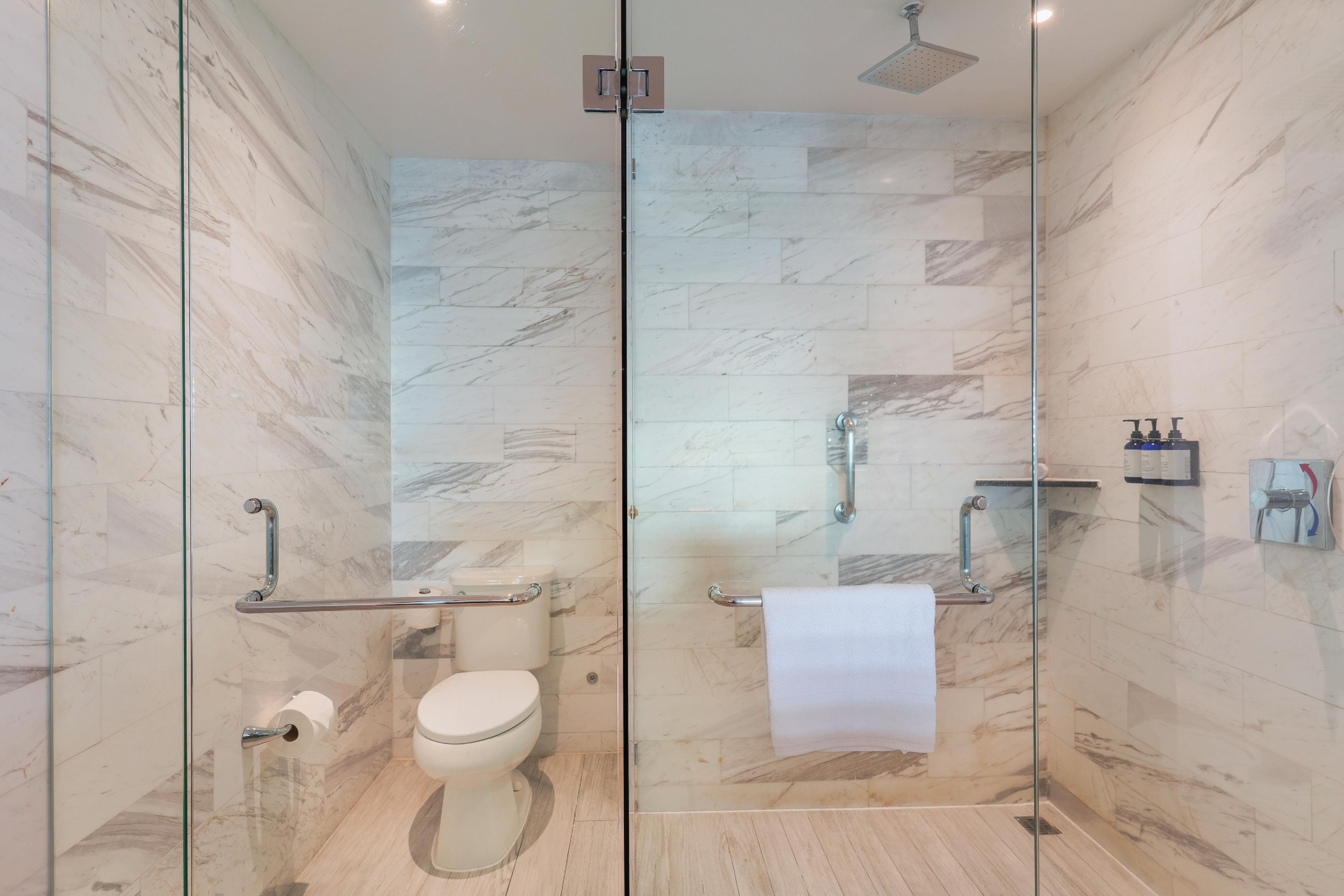 Une salle de bain moderne avec une douche à parois de verre, des murs en marbre, des toilettes et un porte-serviettes.