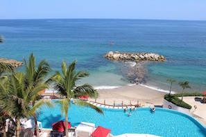 A pool with clear blue water, a sandy beach, and a rocky outcrop in the sea.