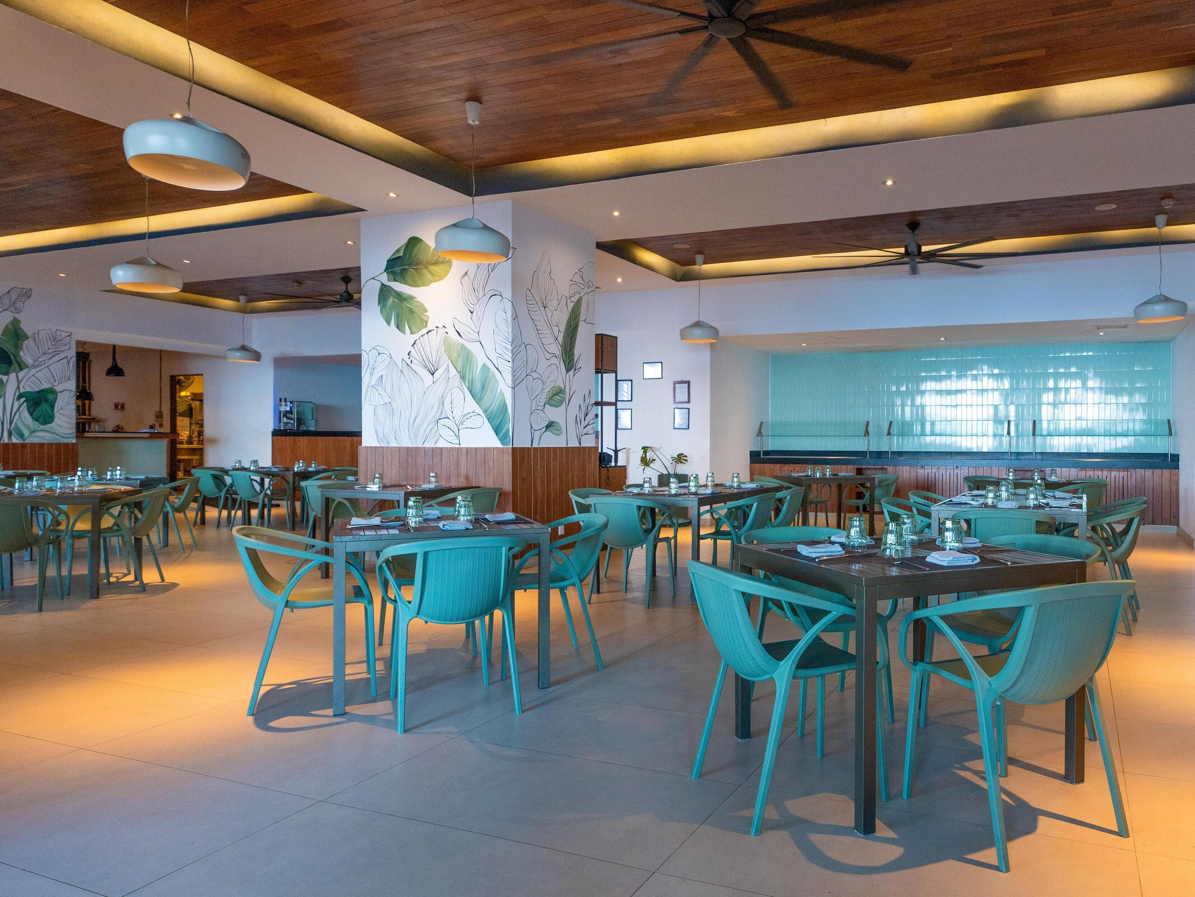 A spacious restaurant with teal chairs and tables, wooden ceiling beams, and wall art.