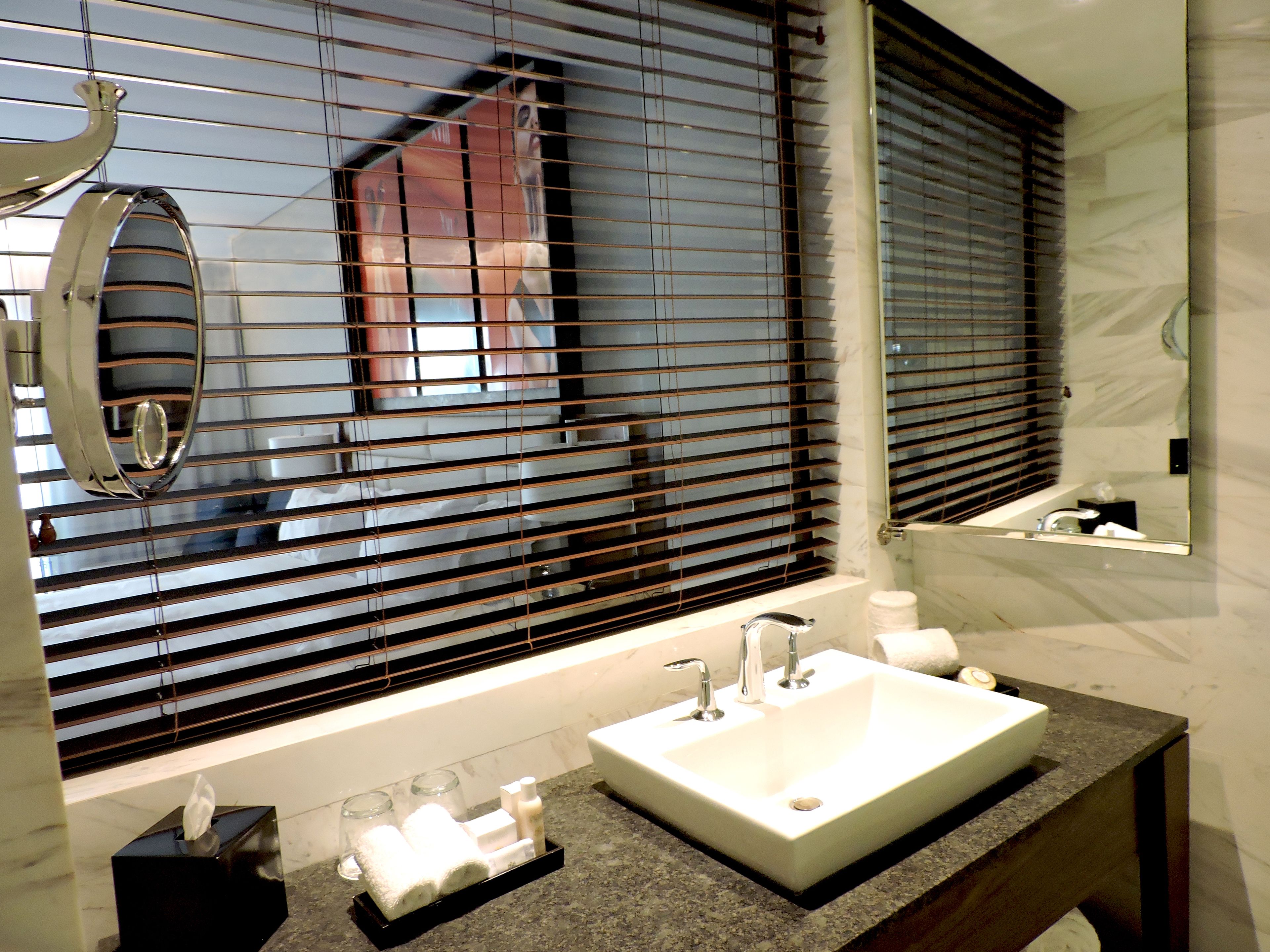 A bathroom with a large sink, a mirror, and a window with blinds.