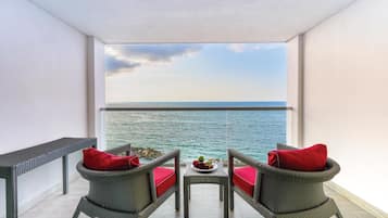 Un balcon avec des fauteuils en osier, une petite table avec des fruits et une vue sur la mer.