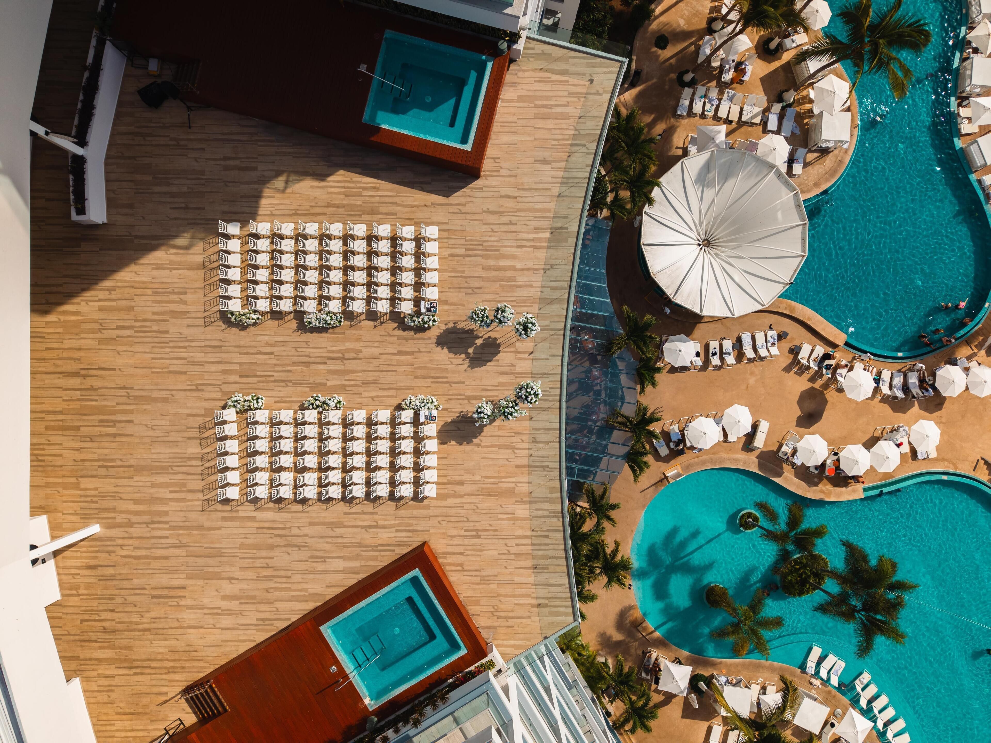 Vista aérea de un complejo turístico con varias piscinas, tumbonas y una zona de terraza de madera.