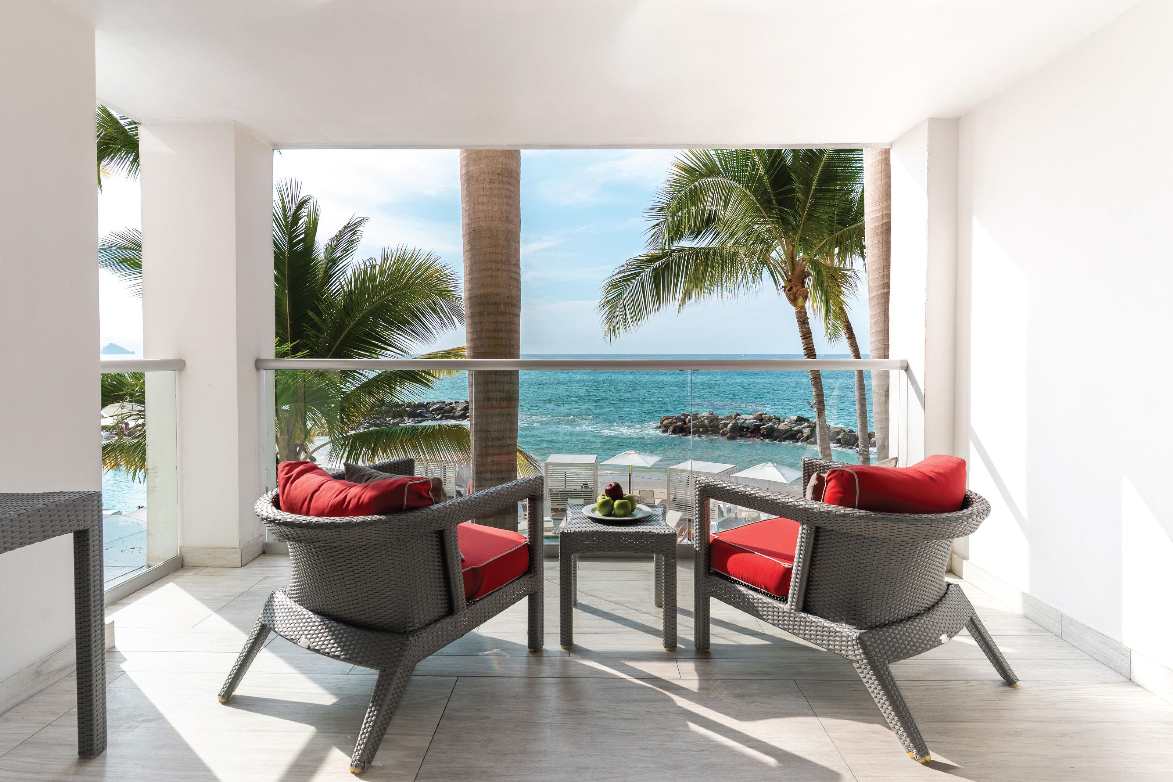 A balcony with wicker furniture, a glass railing, and a view of the ocean.