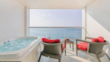 A balcony with a hot tub, wicker chairs with red cushions, and a view of the sea.