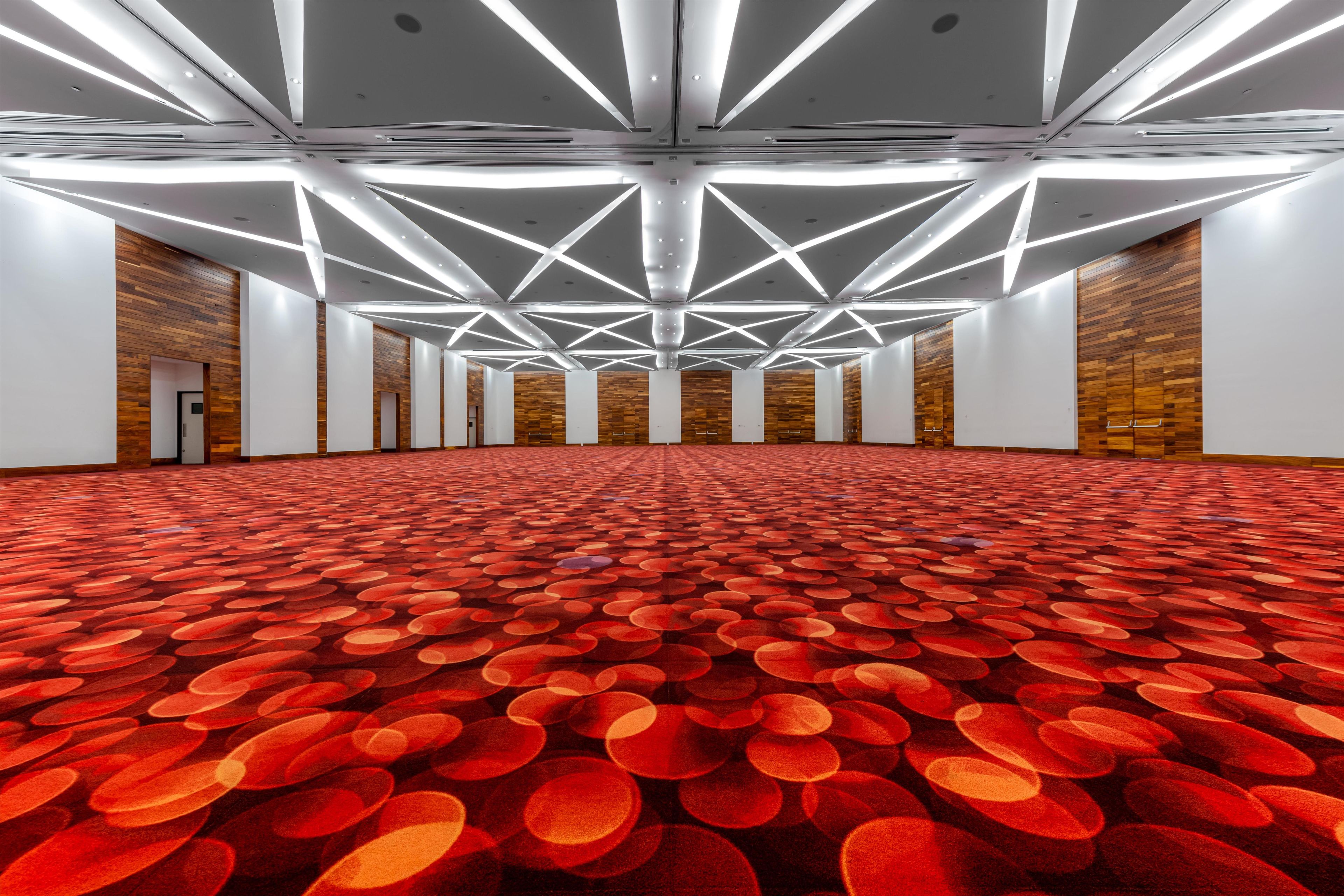 A spacious hall with a patterned carpet, geometric ceiling design, and wooden panel walls.