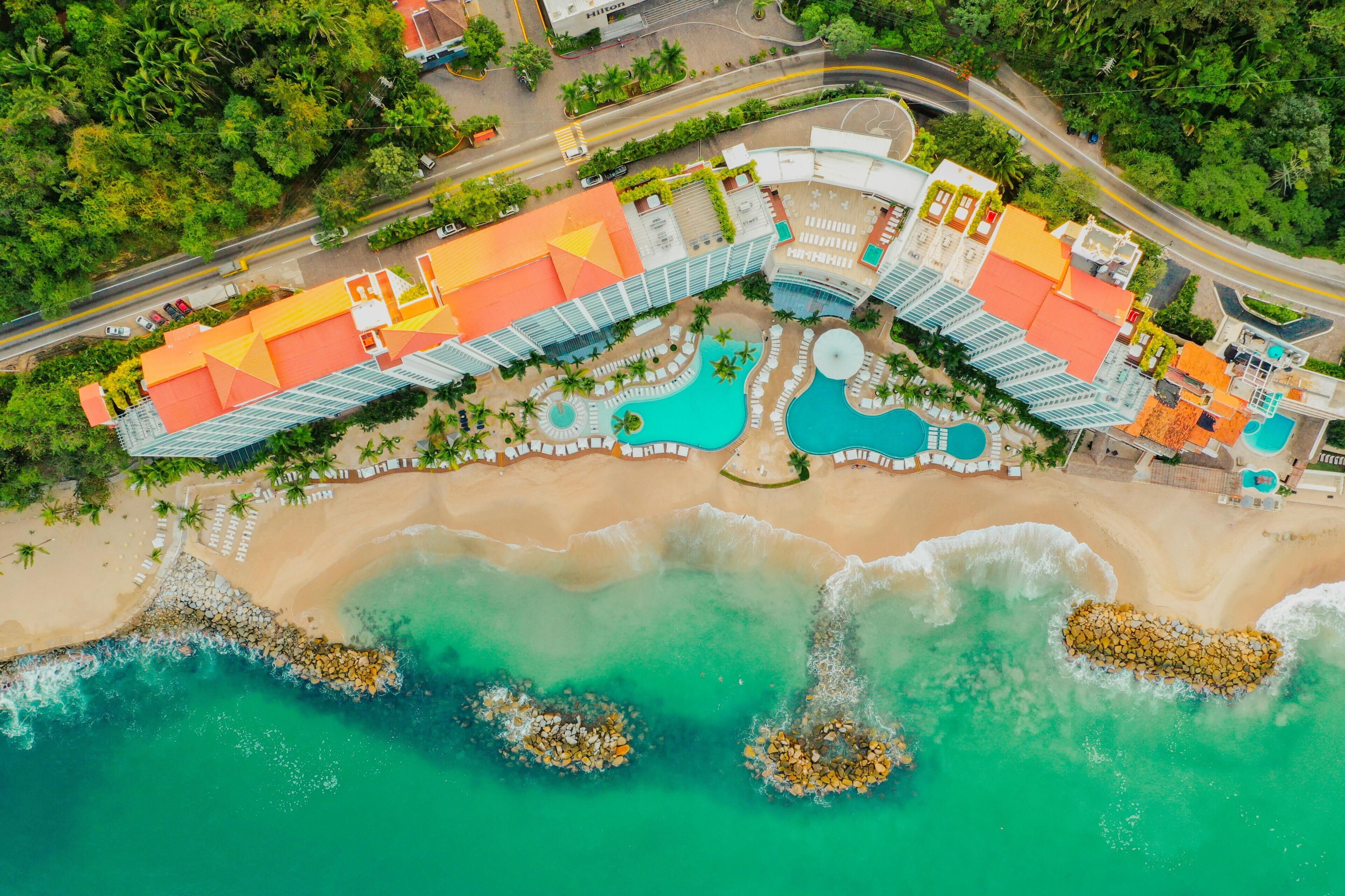 Un complexe hôtelier doté d’une piscine, d’une plage et d’un grand bâtiment dont le toit est incurvé.