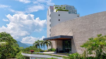 Un hotel moderno con fachada de piedra, techo plano con vegetación y vista al mar.