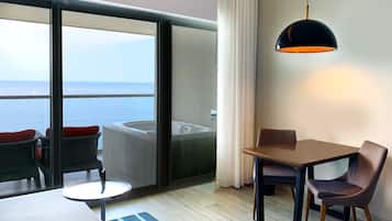 A hotel room with a balcony, a hot tub, a dining table, and a chair.