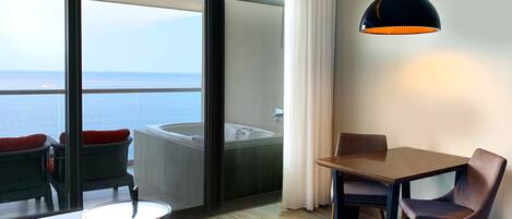 A hotel room with a balcony, a hot tub, a dining table, and a chair.