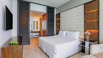 A modern hotel room with a large bed, a flat-screen TV, a wooden desk, and a bathroom visible through an open door.