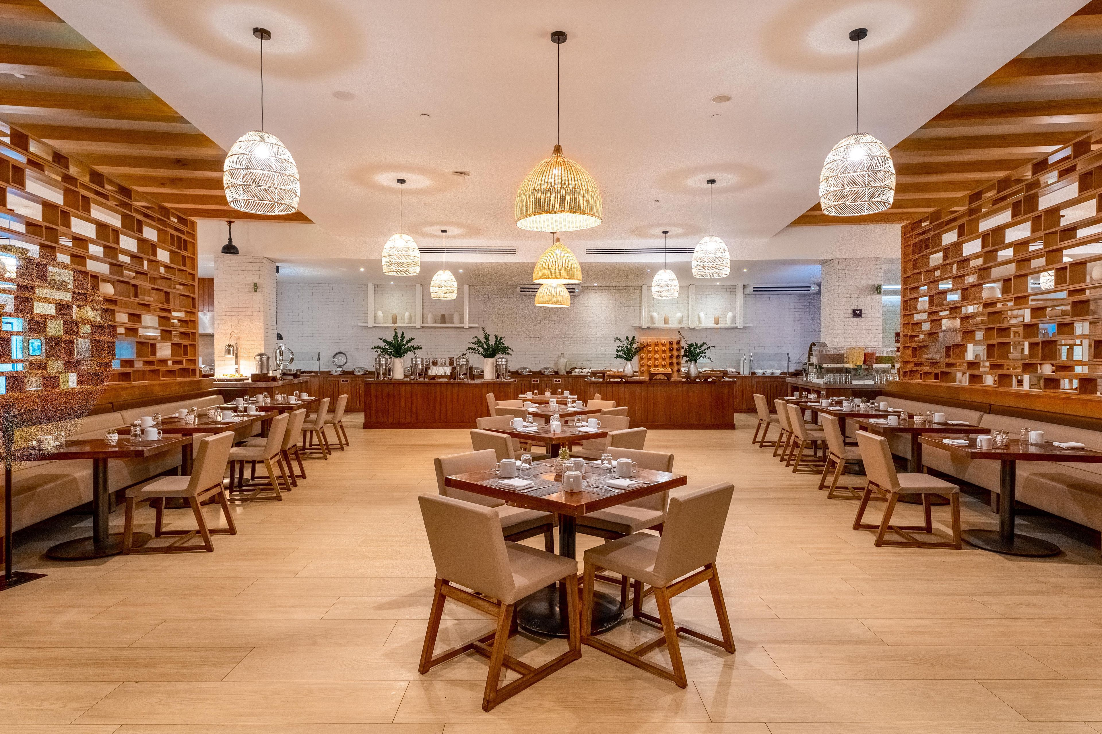 A spacious restaurant with multiple dining tables and chairs, a central bar area, and decorative hanging lights.