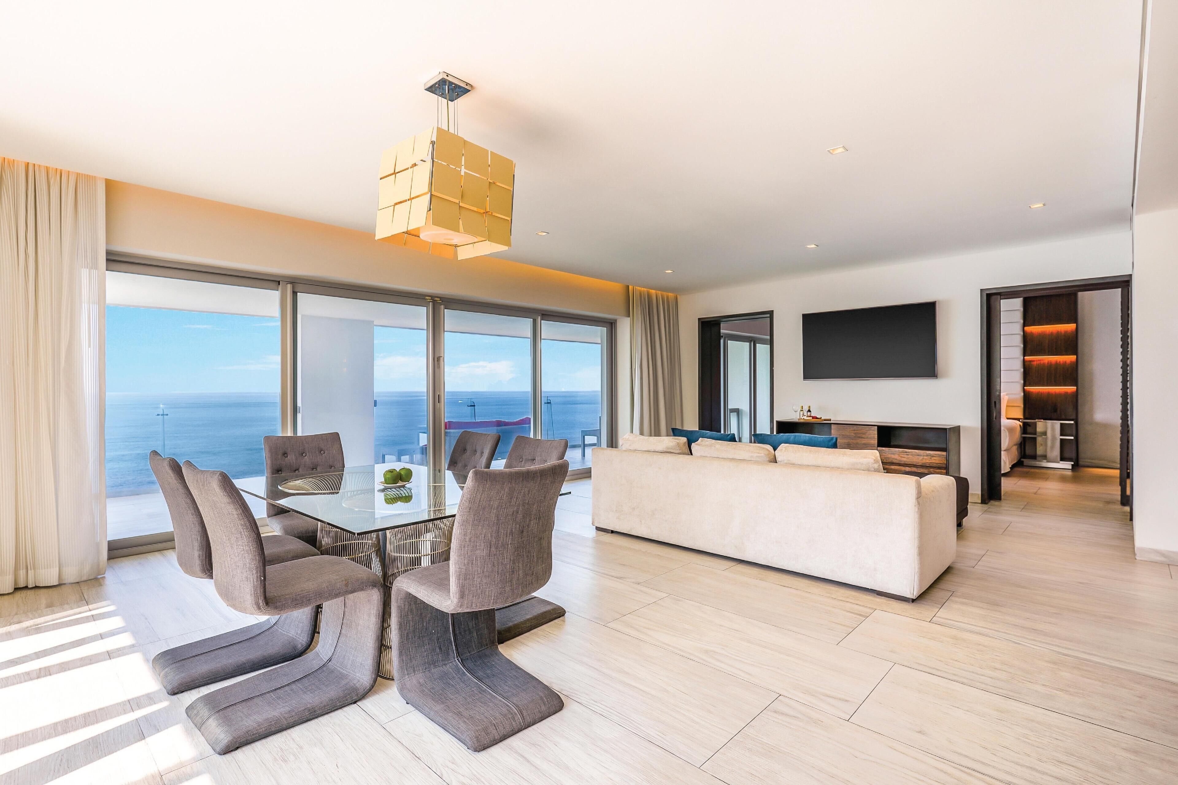 A modern living room with a dining area, large windows, and a flat-screen TV.
