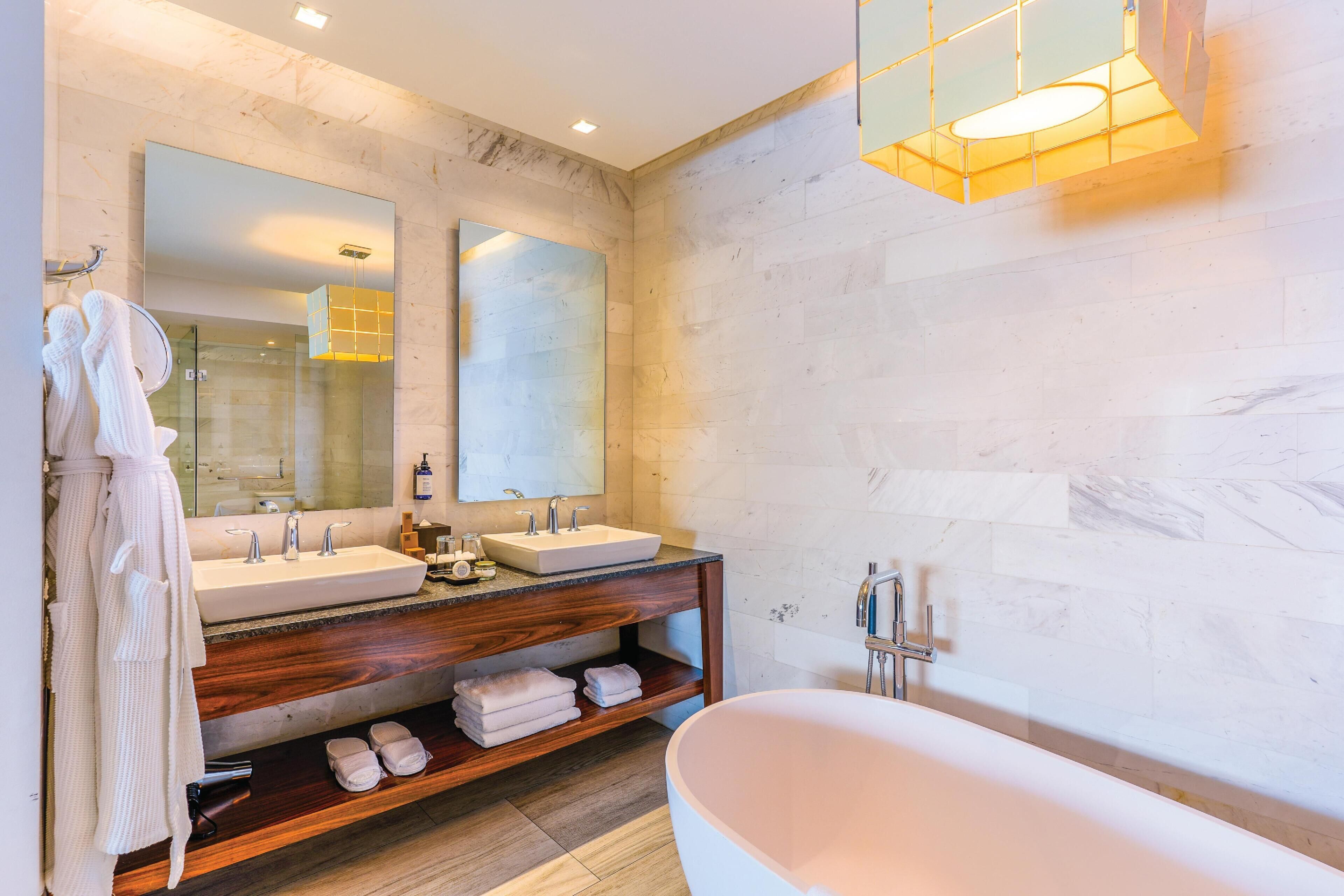 Un baño moderno con dos lavabos, una bañera grande, tocador de madera y un espejo.