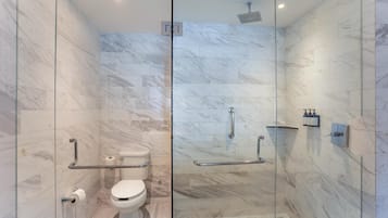 A modern bathroom with a glass partition, marble walls, a toilet, and a shower area.