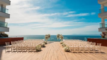 Un salón de bodas en primera línea de playa, con suelo de madera, sillas blancas y decoración floral.