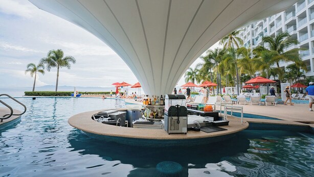 Un área de piscina con bar, sillones y sombrillas.
