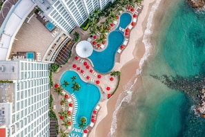 Een resort met meerdere zwembaden, een strand en een hoog gebouw.