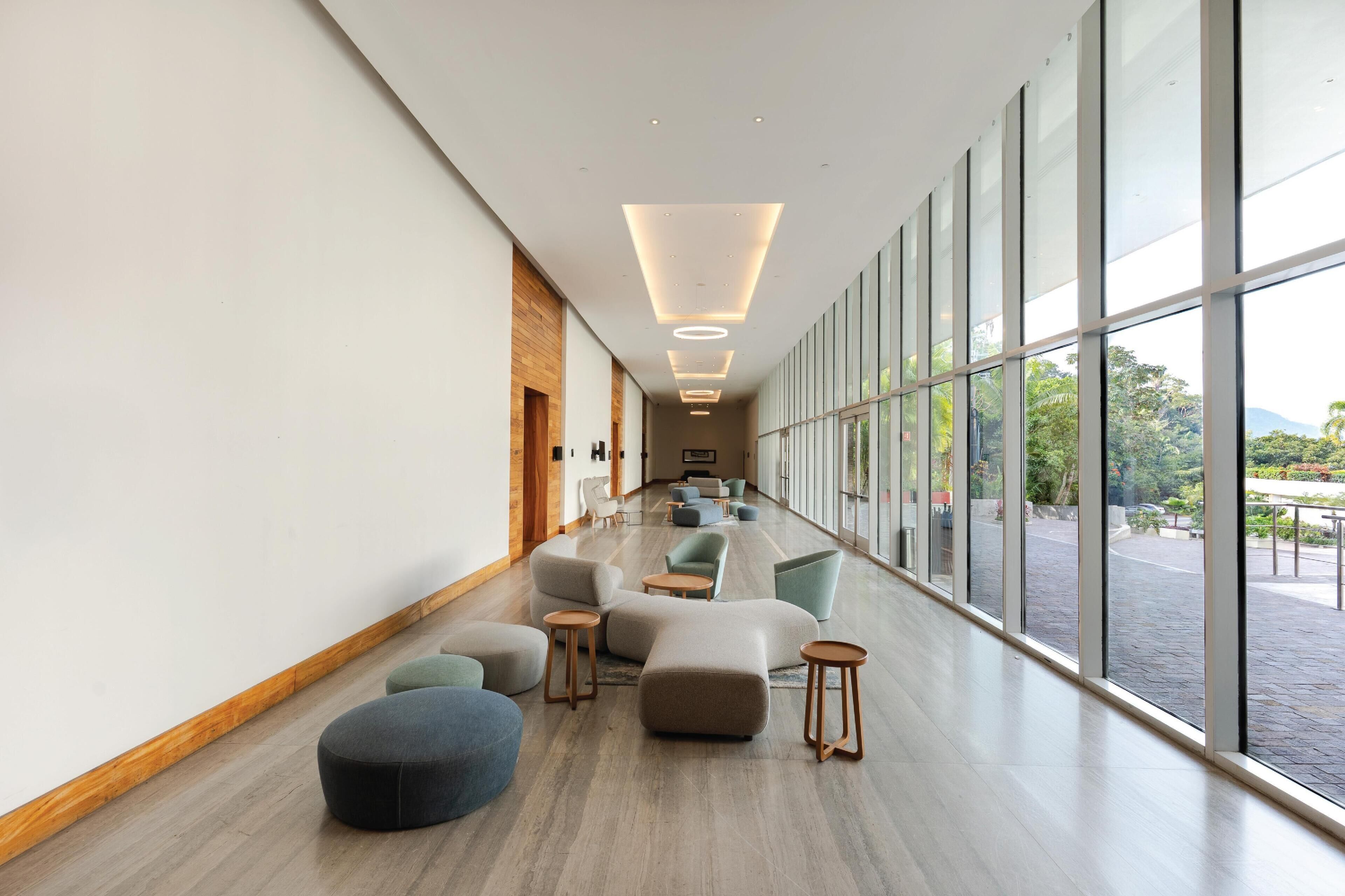Un hall d’hôtel moderne, doté d’un long couloir, de grandes fenêtres et de différents types de sièges.