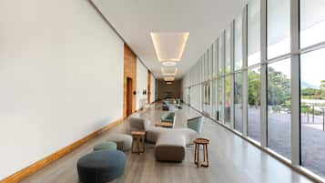Un hall d’hôtel moderne, doté d’un long couloir, de grandes fenêtres et de différents types de sièges.