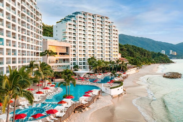 Un hotel con múltiples piscinas, zonas de descanso en la playa y vista al océano.
