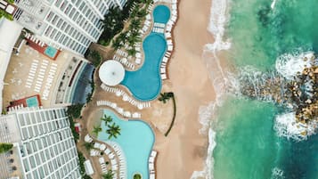 Un resort con varias piscinas, una playa y un edificio grande con balcones.