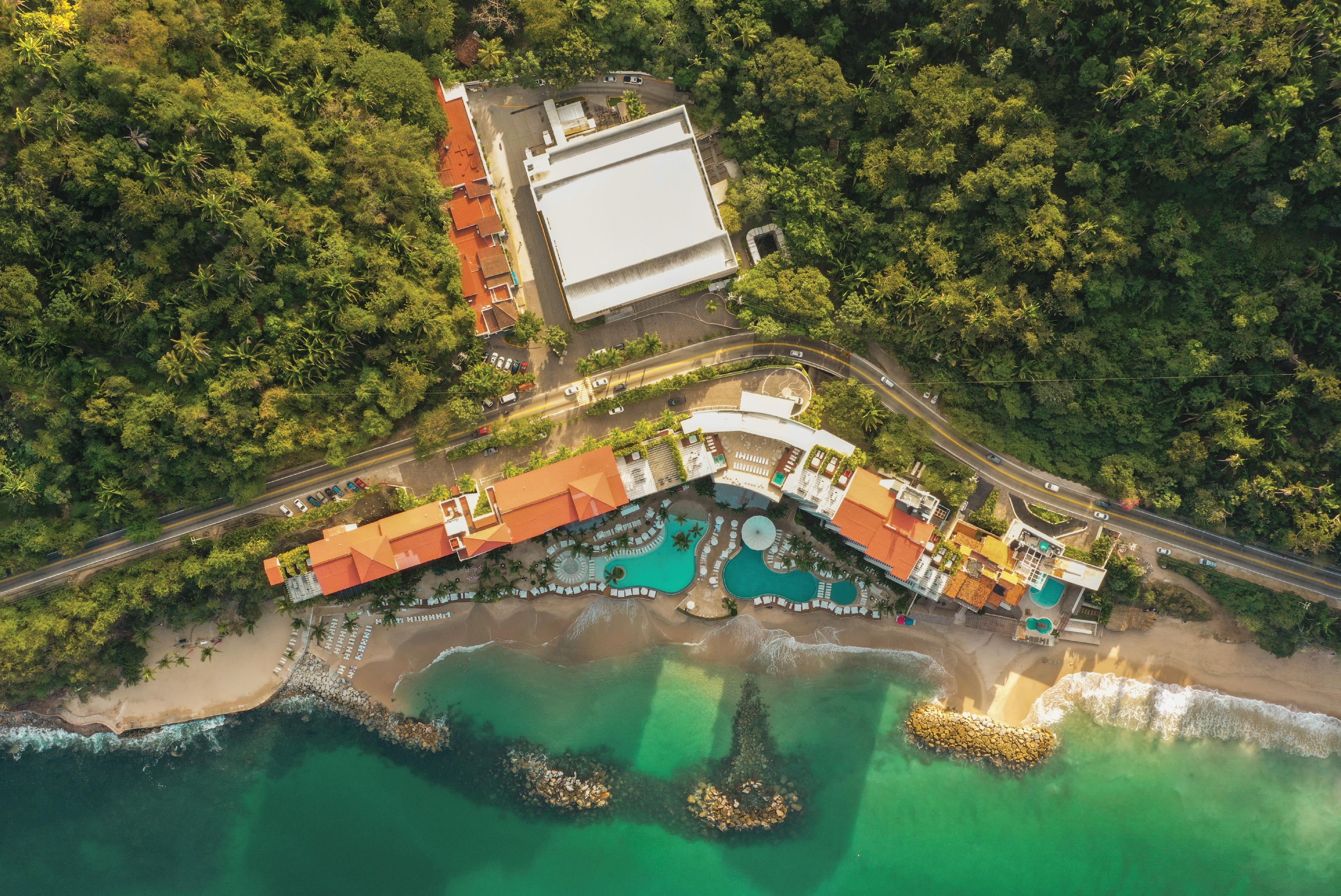 An aerial view of a resort with a beach, swimming pools, and a large building.