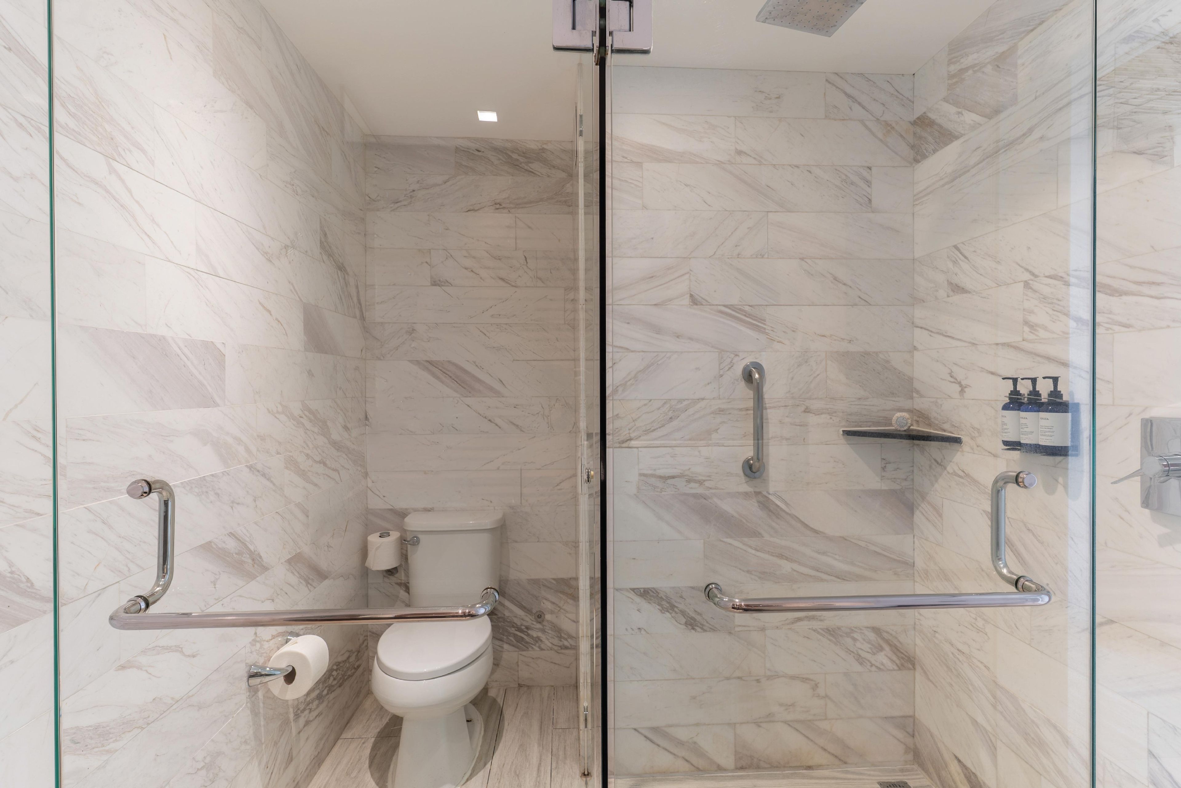 Un bagno moderno con cabina doccia in vetro, un water con maniglione e pavimento in marmo.