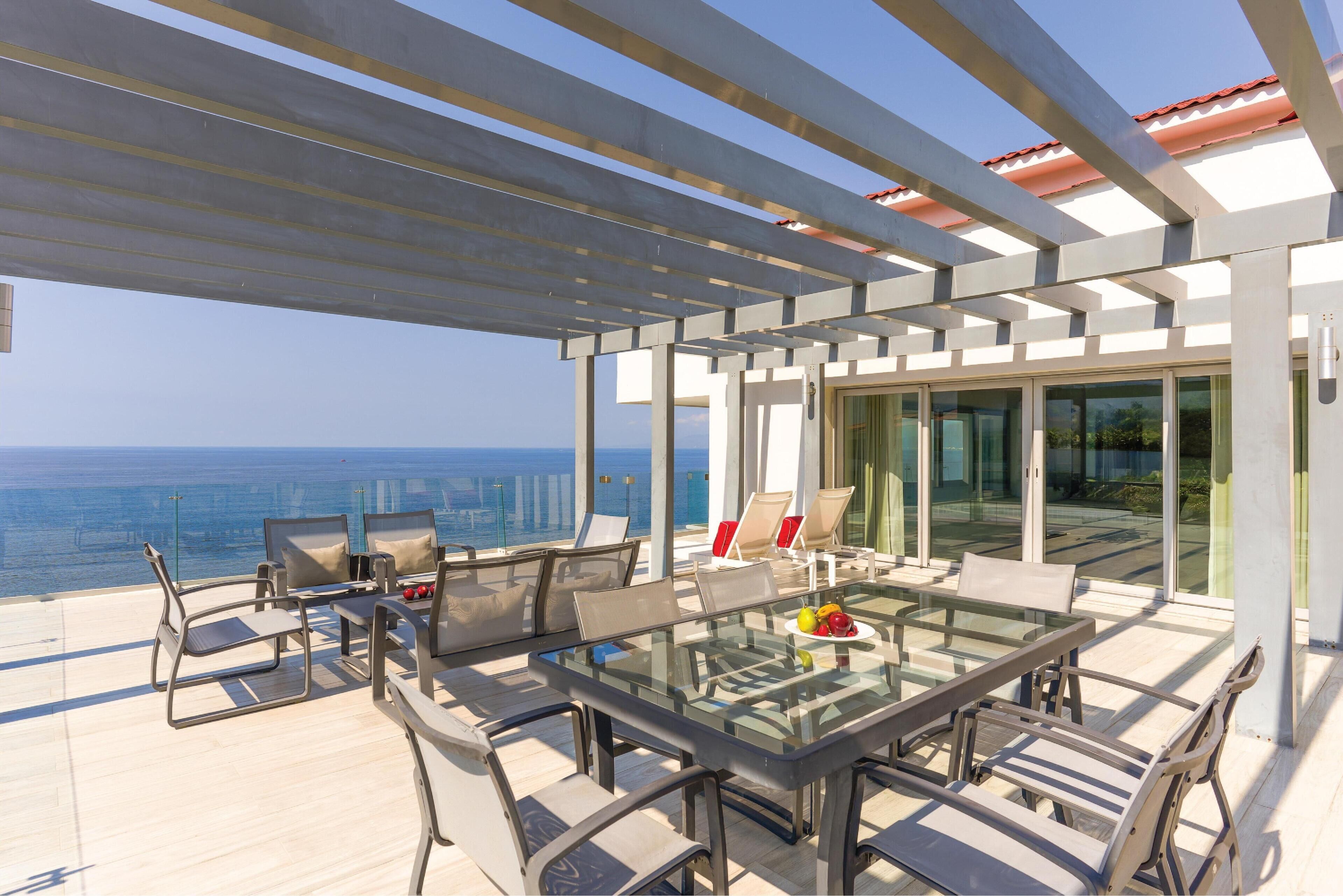 A modern outdoor patio with a glass table and chairs, overlooking a cityscape.