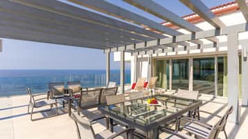 A modern outdoor patio with a glass table and chairs, overlooking a cityscape.