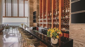 A bar area with a long counter, wicker chairs, and a view of the ocean.