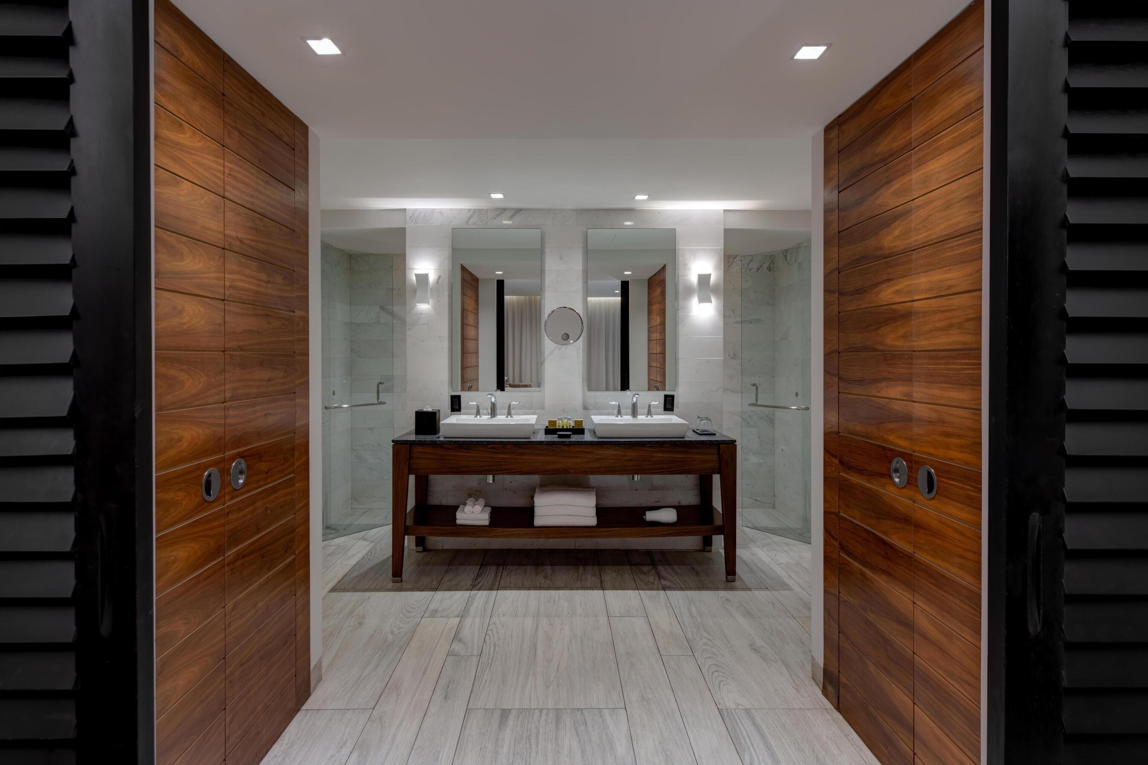 A modern bathroom with a wooden vanity, two sinks, and a large mirror.