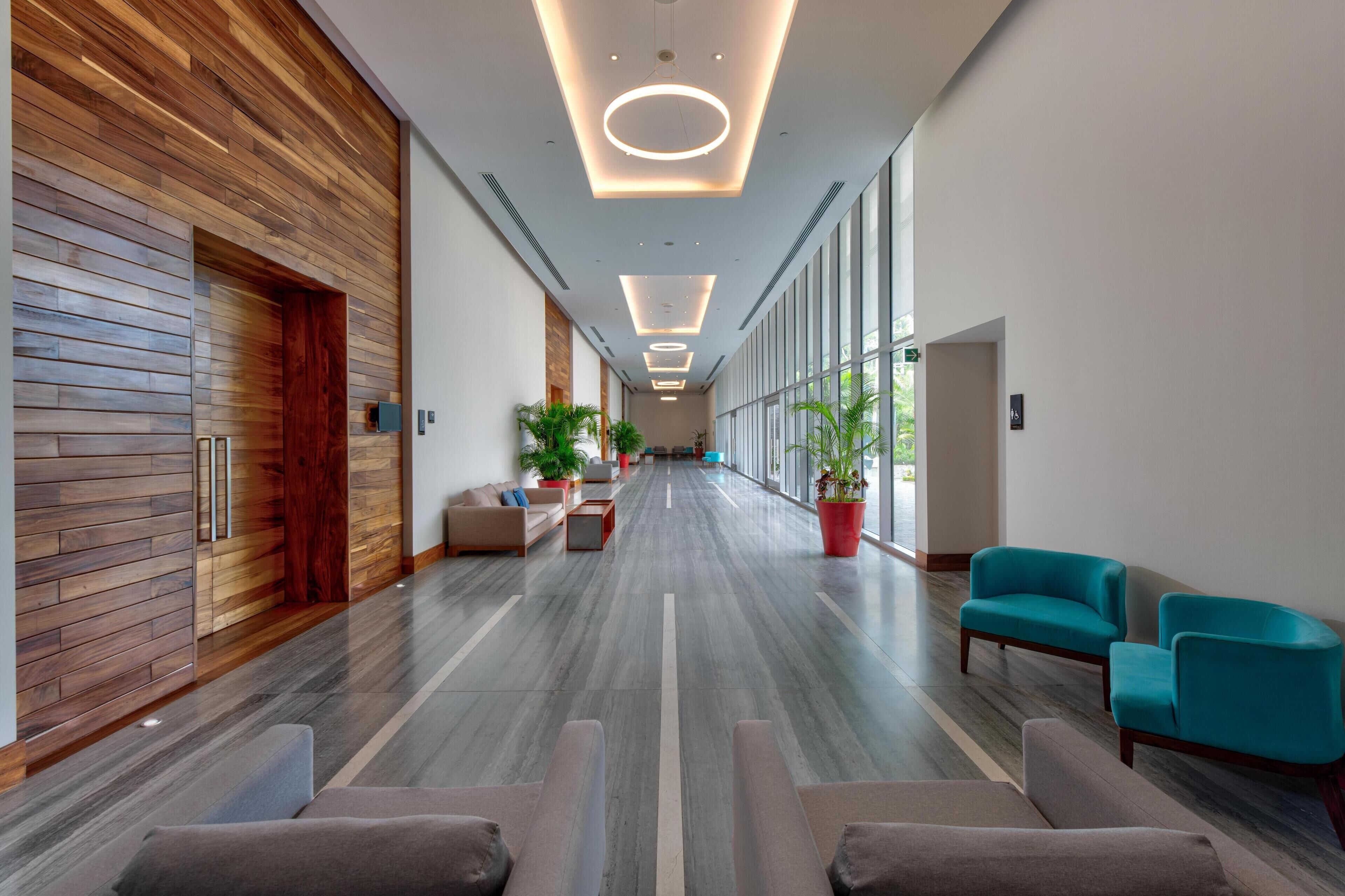A modern lobby with a wooden wall, a long corridor, and seating areas with teal chairs.