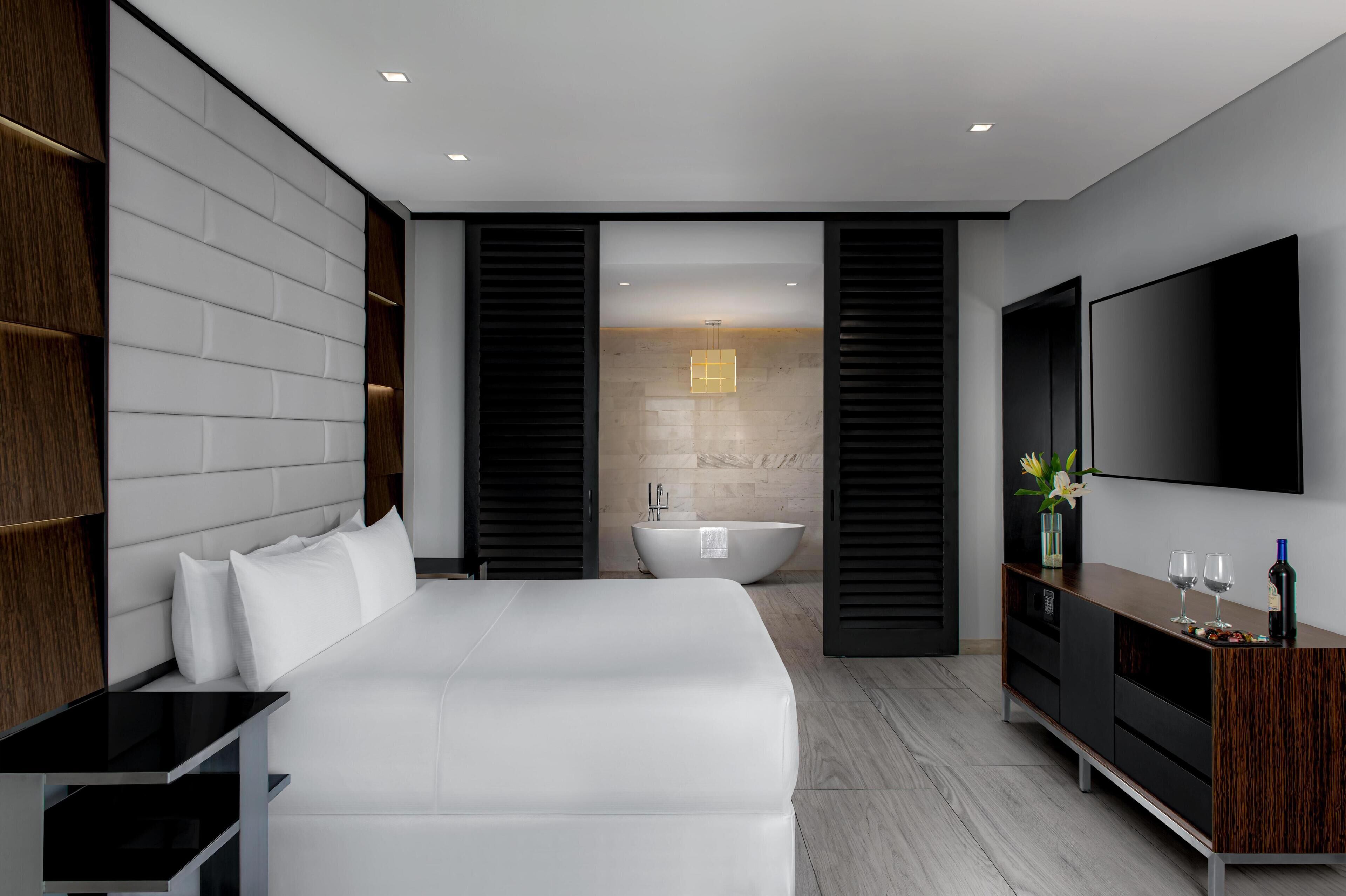 Ein modernes Hotelzimmer mit einem großen Bett, einem Flachbildfernseher, einer Holzkommode und einer Badewanne.