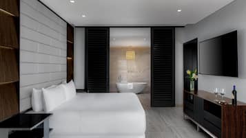A modern hotel room with a large bed, a flat-screen TV, a wooden cabinet, and a bathtub.