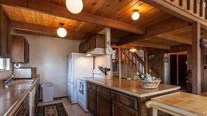 A rustic kitchen with wooden cabinets, a refrigerator, a microwave, and a sink. There is a wooden staircase leading to another level. - Pinnacle View (Truckee)