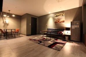 A modern living room with a sofa, a dining table with chairs, a rug, and a refrigerator. - Hotel Banwol (Uijeongbu)