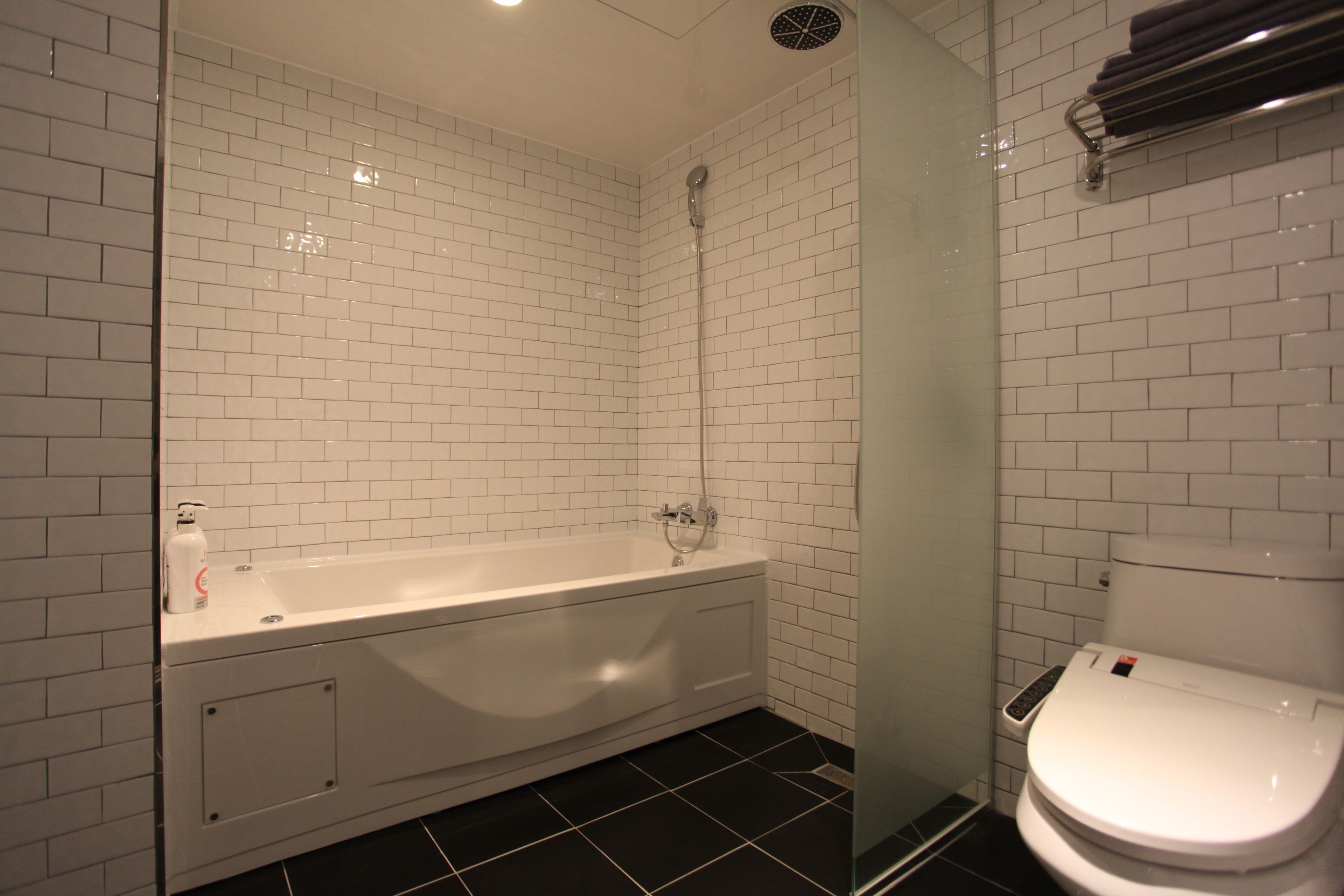 Un baño con paredes de azulejos blancos, una bañera blanca, una cabina de ducha de vidrio y un inodoro blanco.