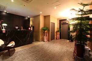 Zona de recepción de hotel con mostrador de mármol, paneles de madera y plantas en macetas.