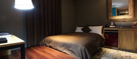 A hotel room with a bed, bedside table, lamp, mirror, and a small sink.