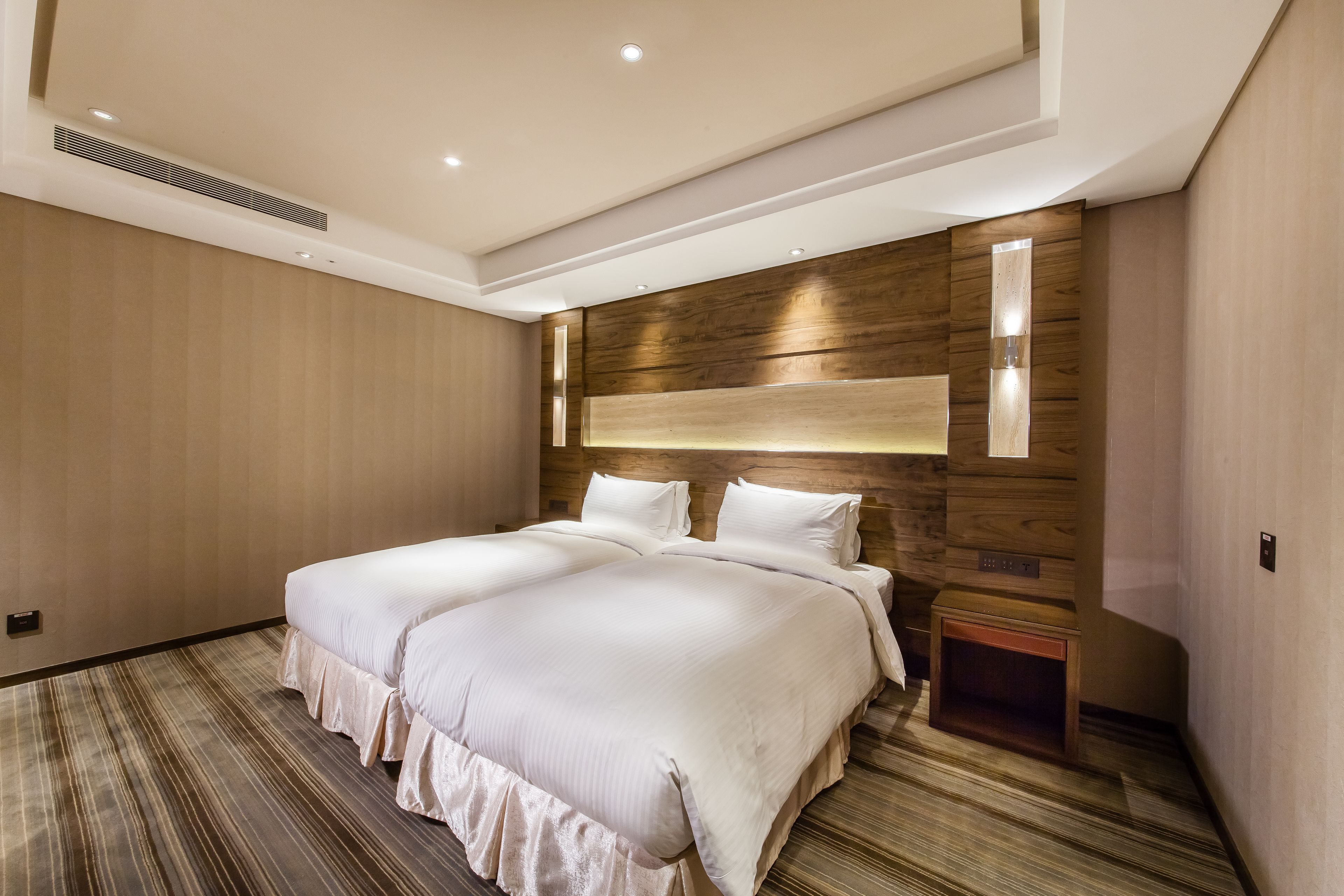 Una habitación de hotel moderna con una cama grande, paneles de madera en las paredes y una mesita de noche pequeña.