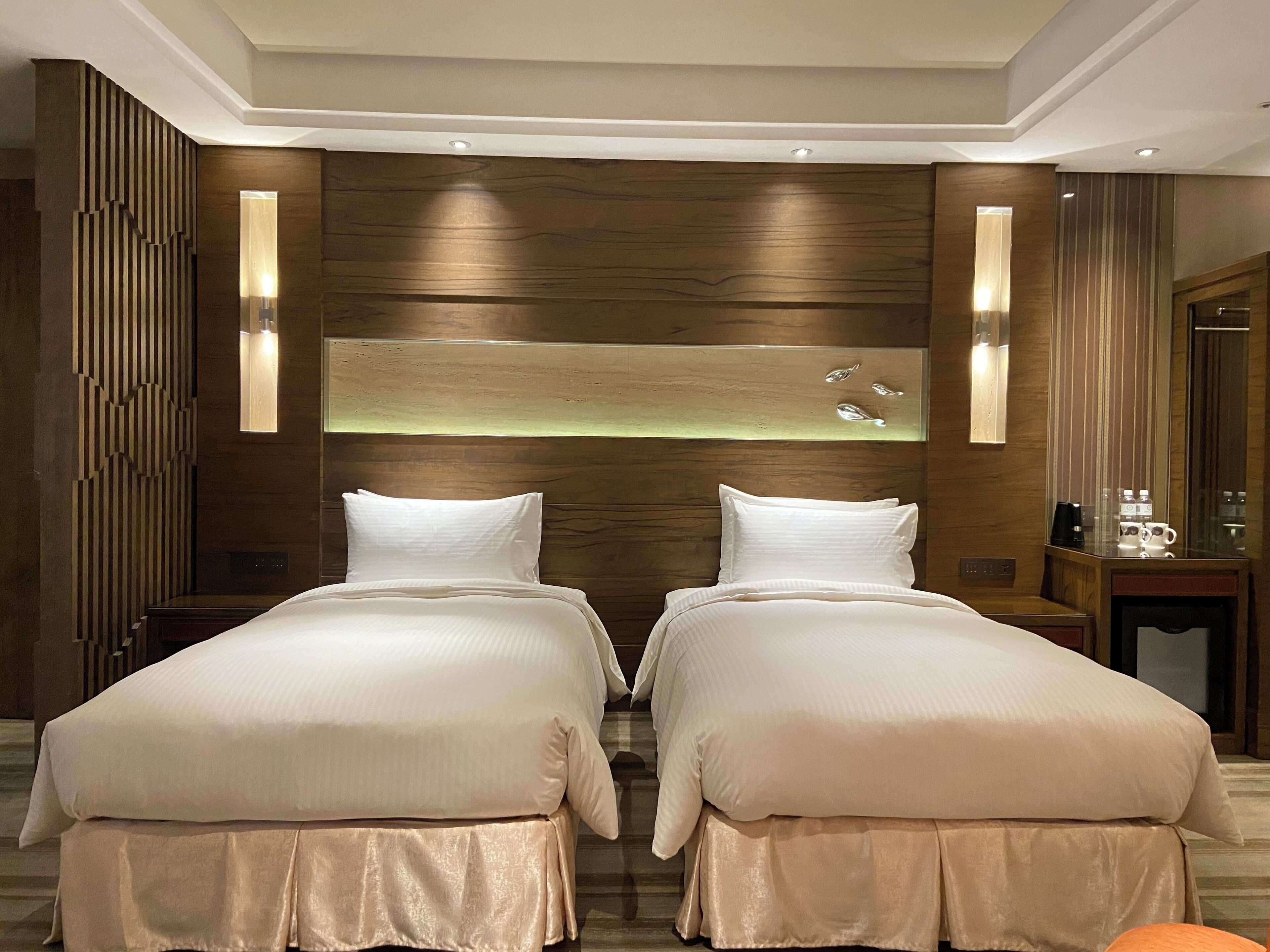 A hotel room with two beds, wooden paneling, a nightstand with a lamp, and a mirror.