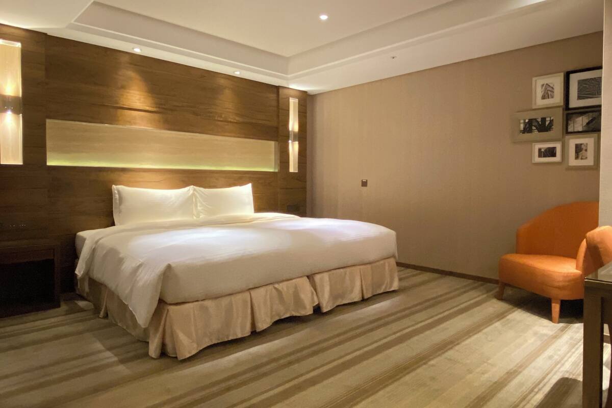 A hotel room with a large bed, a wooden headboard, a chair, and framed pictures on the wall.