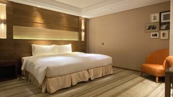 A hotel room with a large bed, a wooden headboard, a chair, and framed pictures on the wall.