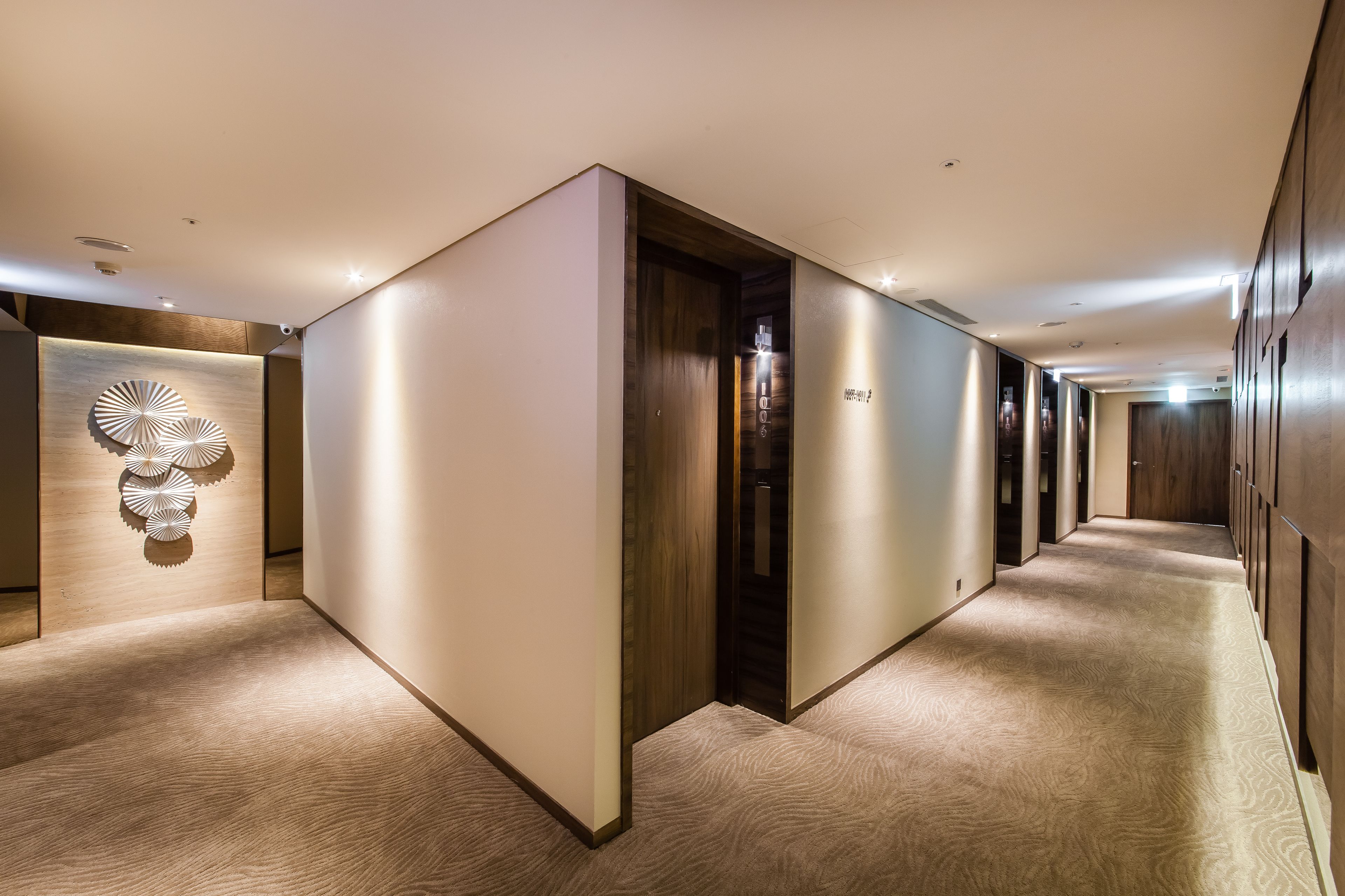 A modern hotel corridor with wooden paneling, a carpeted floor, and a wall-mounted light fixture.