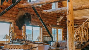 Interior rústico de una cabaña con vigas de madera, una escultura de oso, astas de ciervo y un rincón de estar acogedor.