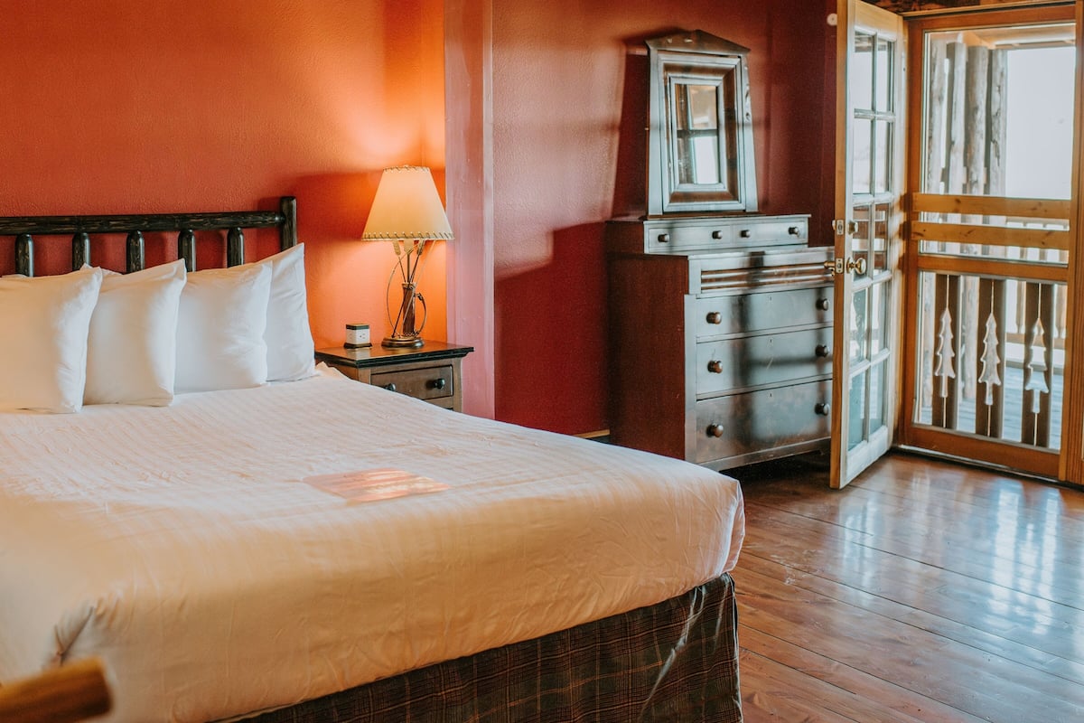 A hotel room with a large bed, a nightstand with a lamp, a dresser, and a door leading to a balcony.