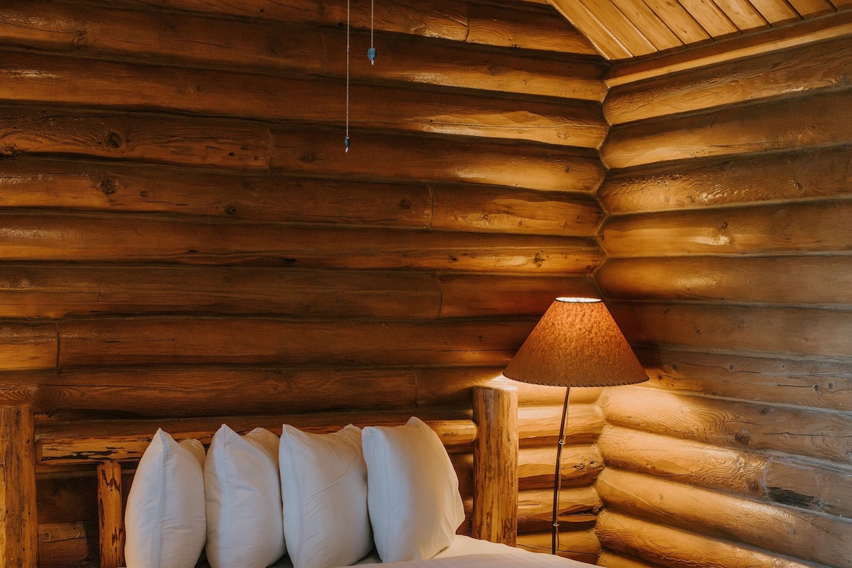 A log cabin room with a wooden bed, a lamp, and a wooden headboard.